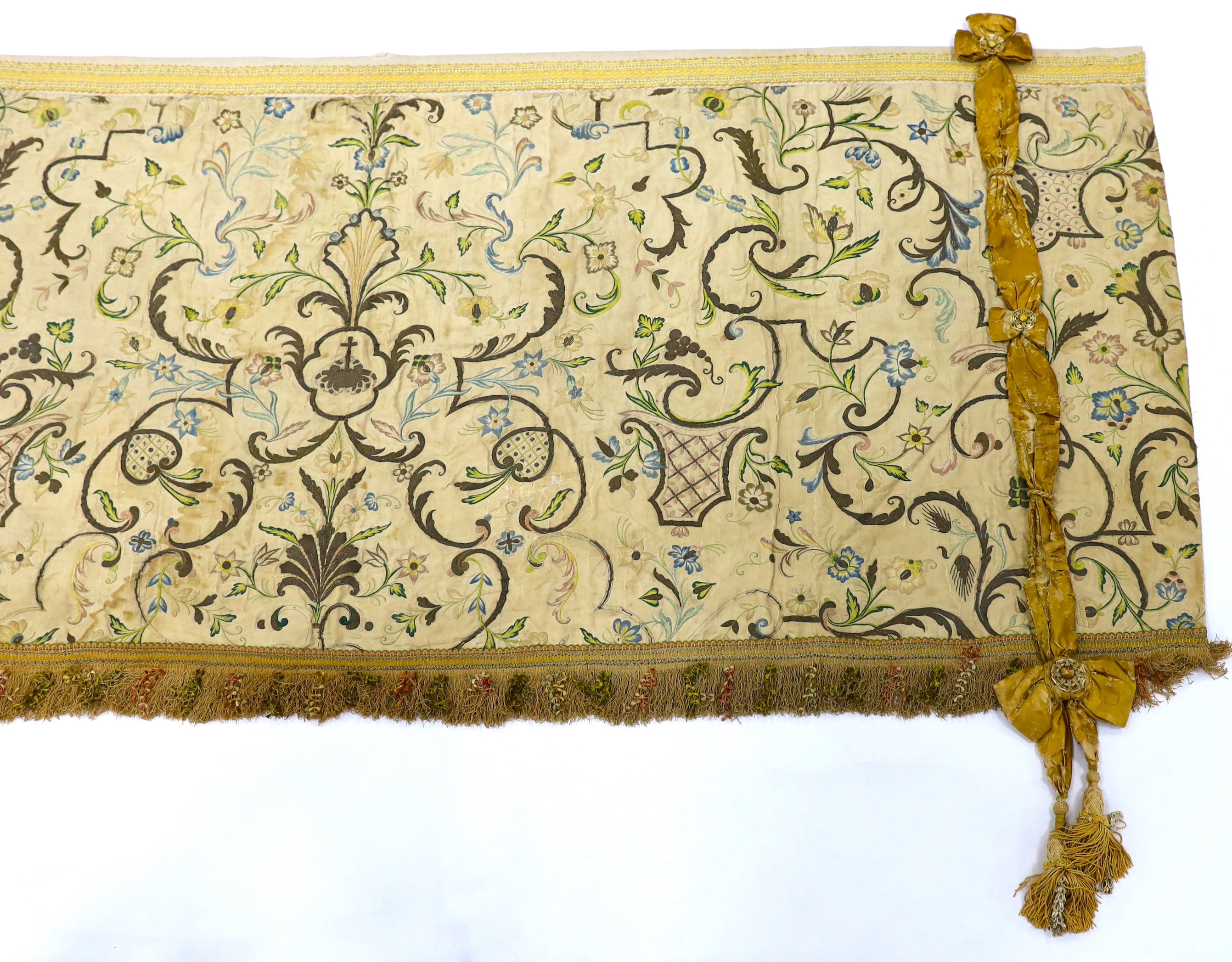 A mid-18th century Continental silk embroidered altar cloth, embroidered with polychrome silks and silver metallic threads in an all-over floral design on cream silk with ornate silk tasselling, (the damask tie backs add